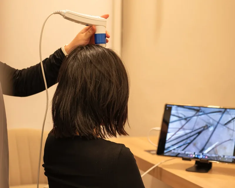 A scalp camera resting on a guest’s scalp, with the magnified image of her hair and scalp on the screen beside her