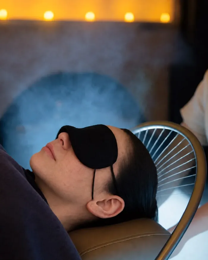 A guest resting with an eye mask under the waterfall halo, candlelight above her