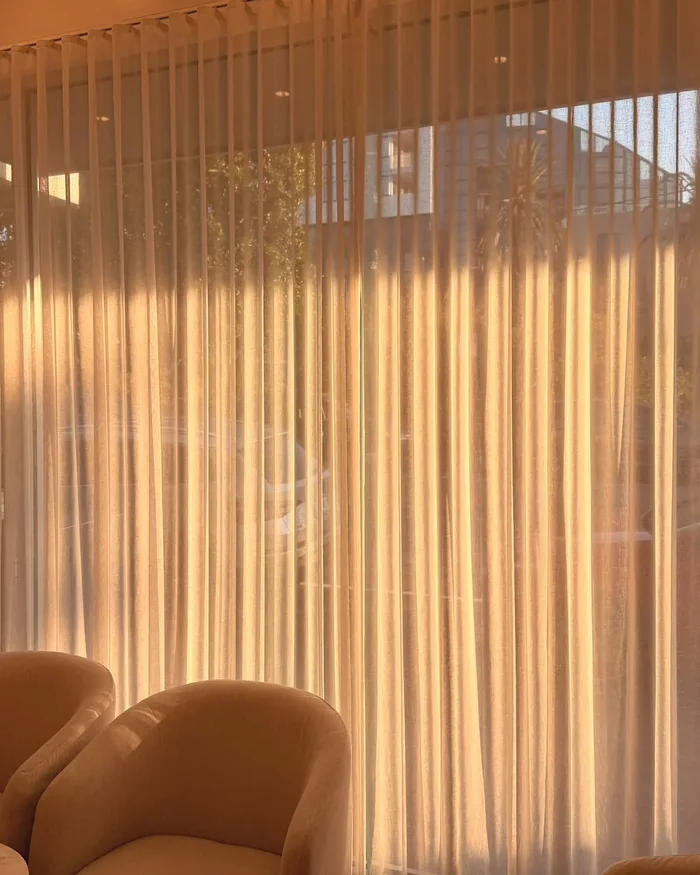 Sunlight through sheer curtains onto two armchairs at the front of Hikari