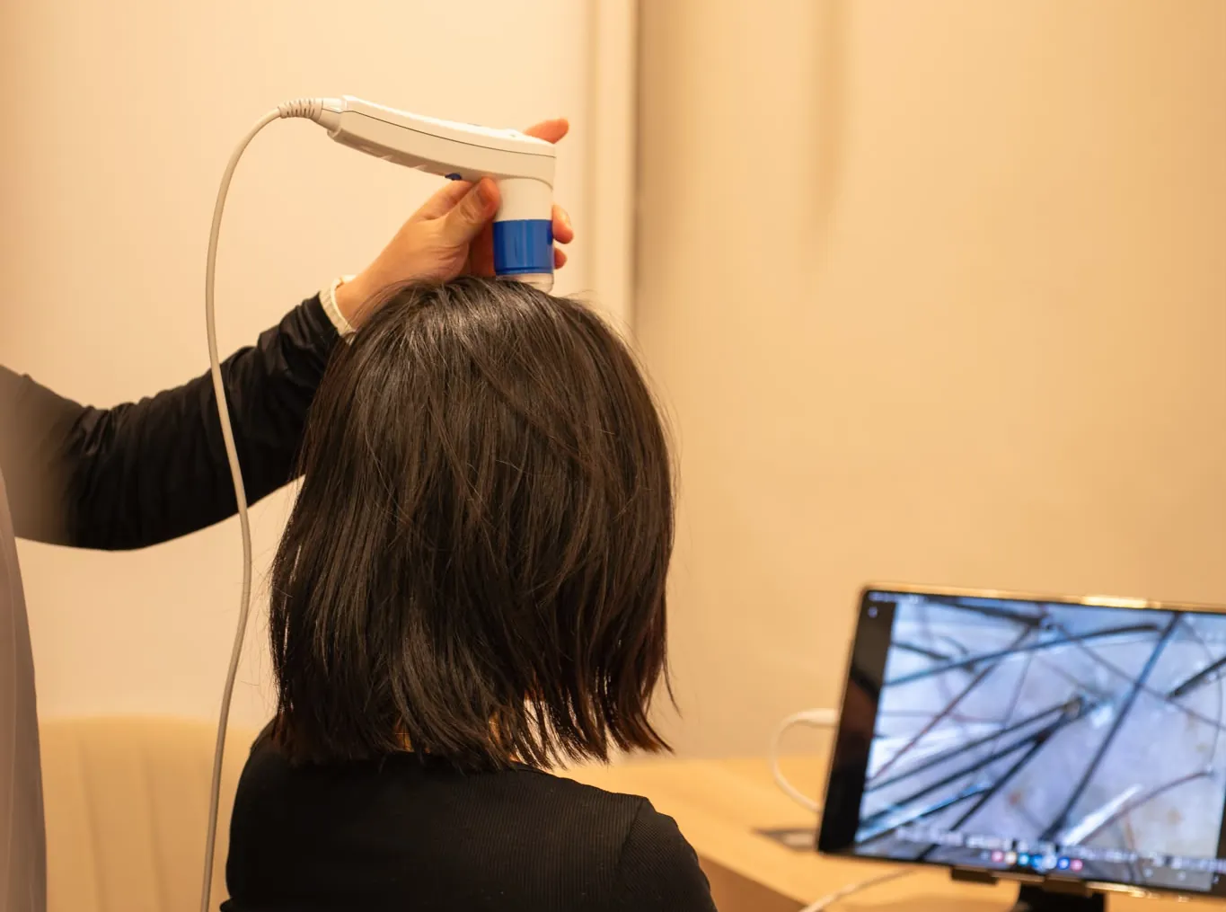 A scalp camera assessment at Hikari: the camera rests on the guest’s scalp while a magnified view of the hair and scalp shows on the screen beside her